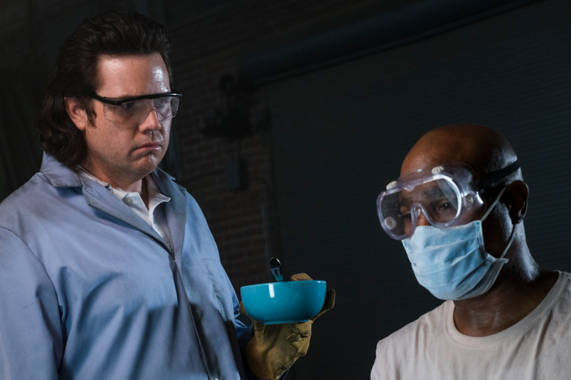 Father Gabriel (Seth Gilliam, right) may be ill and forced to make weapons designed to kill his friends, but at least his mask protects him from the smell of Eugene’s (Josh McDermitt) dinner.